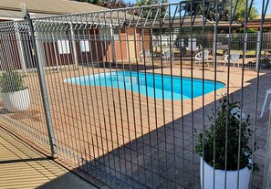 A swimming pool surrounded by a metal fence, with a brick patio and white plastic chairs. - Centrepoint Motel (Deniliquin)