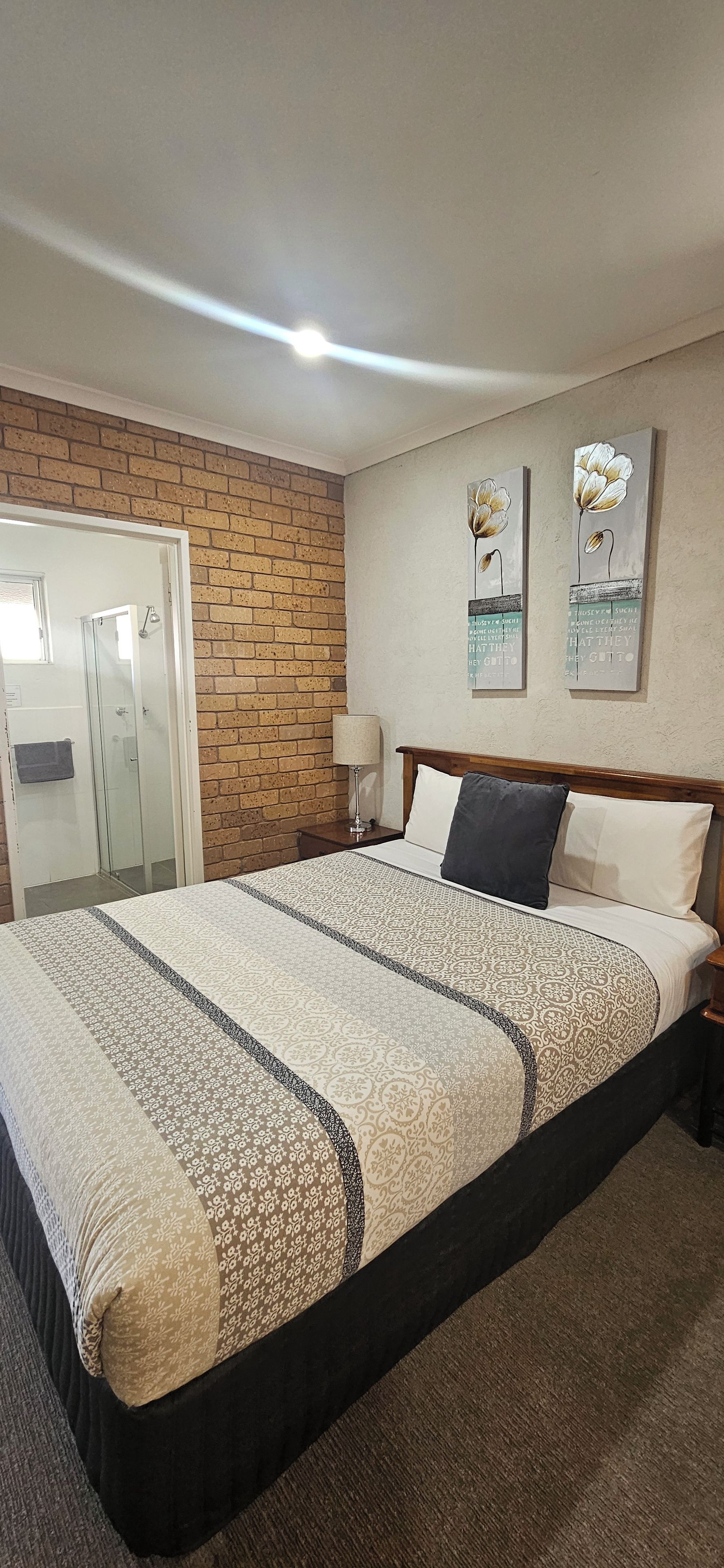 Habitación de hotel con una cama grande, una pared decorada con ladrillos, una mesita de noche con lámpara y dos obras de arte en la pared.