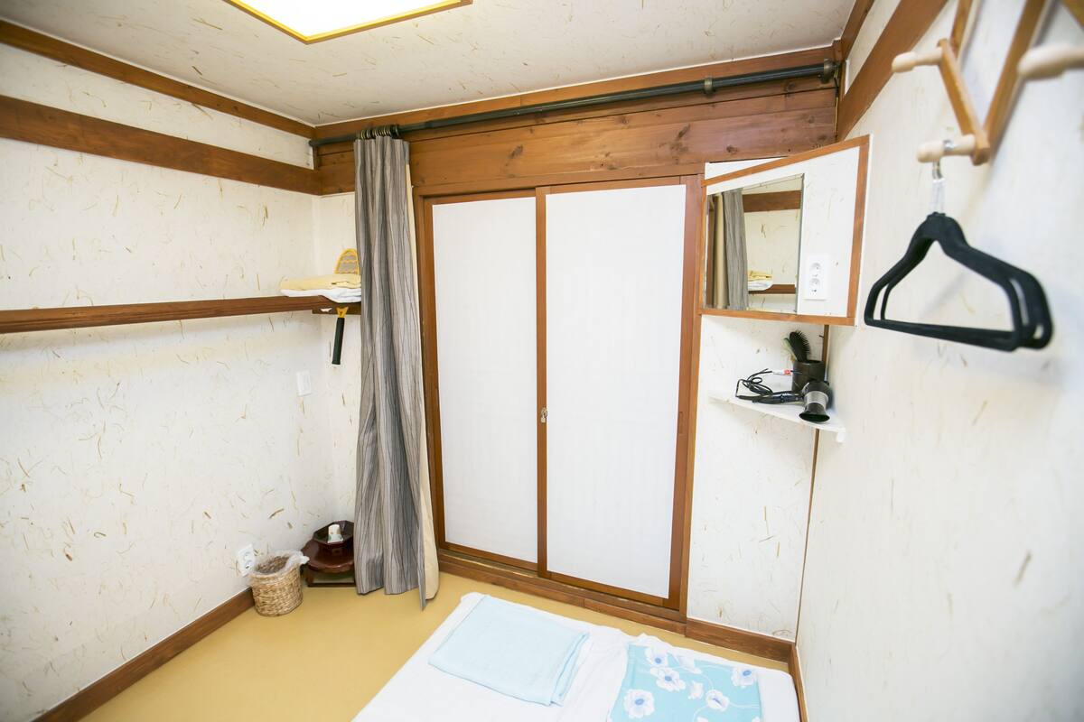 Een traditionele Japanse kamer met tatami vloerbedekking, een shoji schuifdeur, een houten balkenplafond en een zwarte hangende kapstok.
