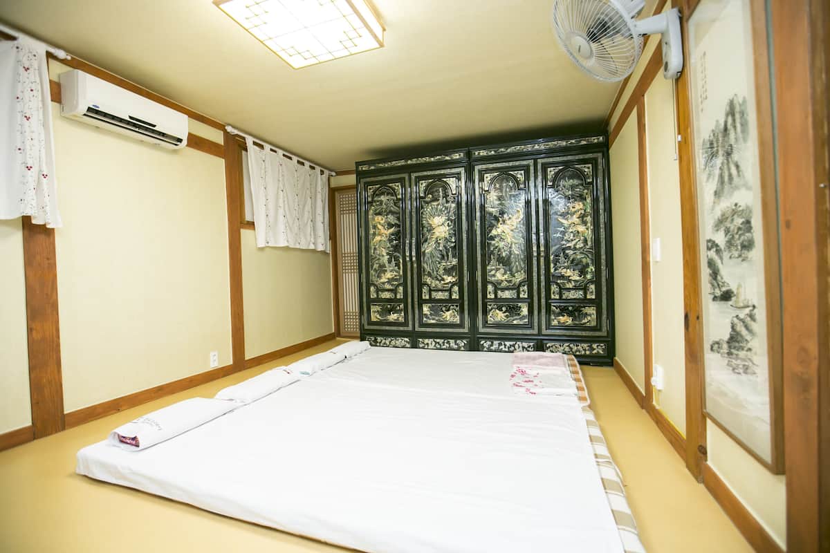 Een kamer met een bed, een airconditioner, een ventilator en een raam met uitzicht op bomen.