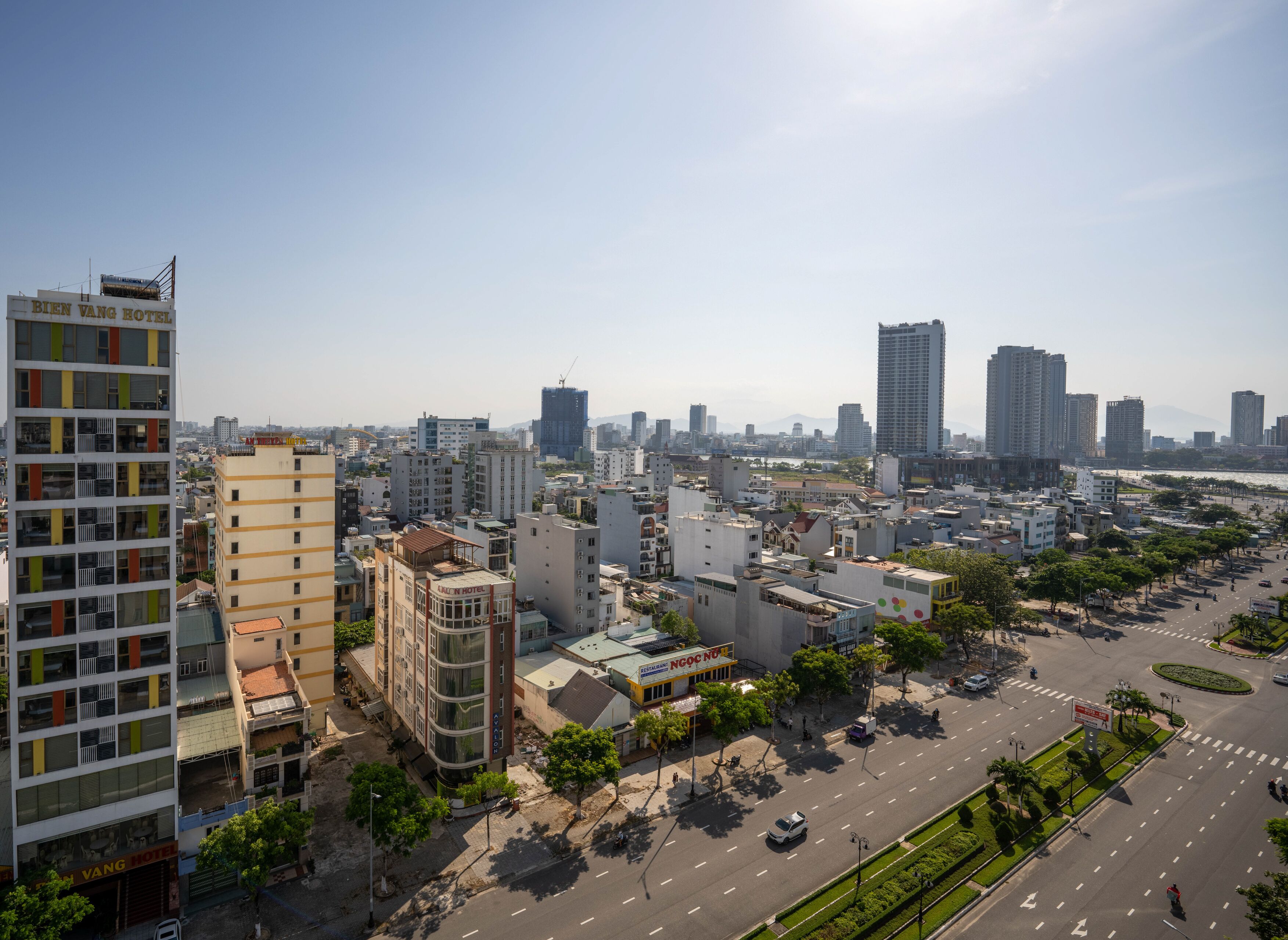 Une vue sur la ville avec un hôtel imposant appelé « Bien Vang Hotel », qui présente un design moderne avec de nombreux étages et des balcons.