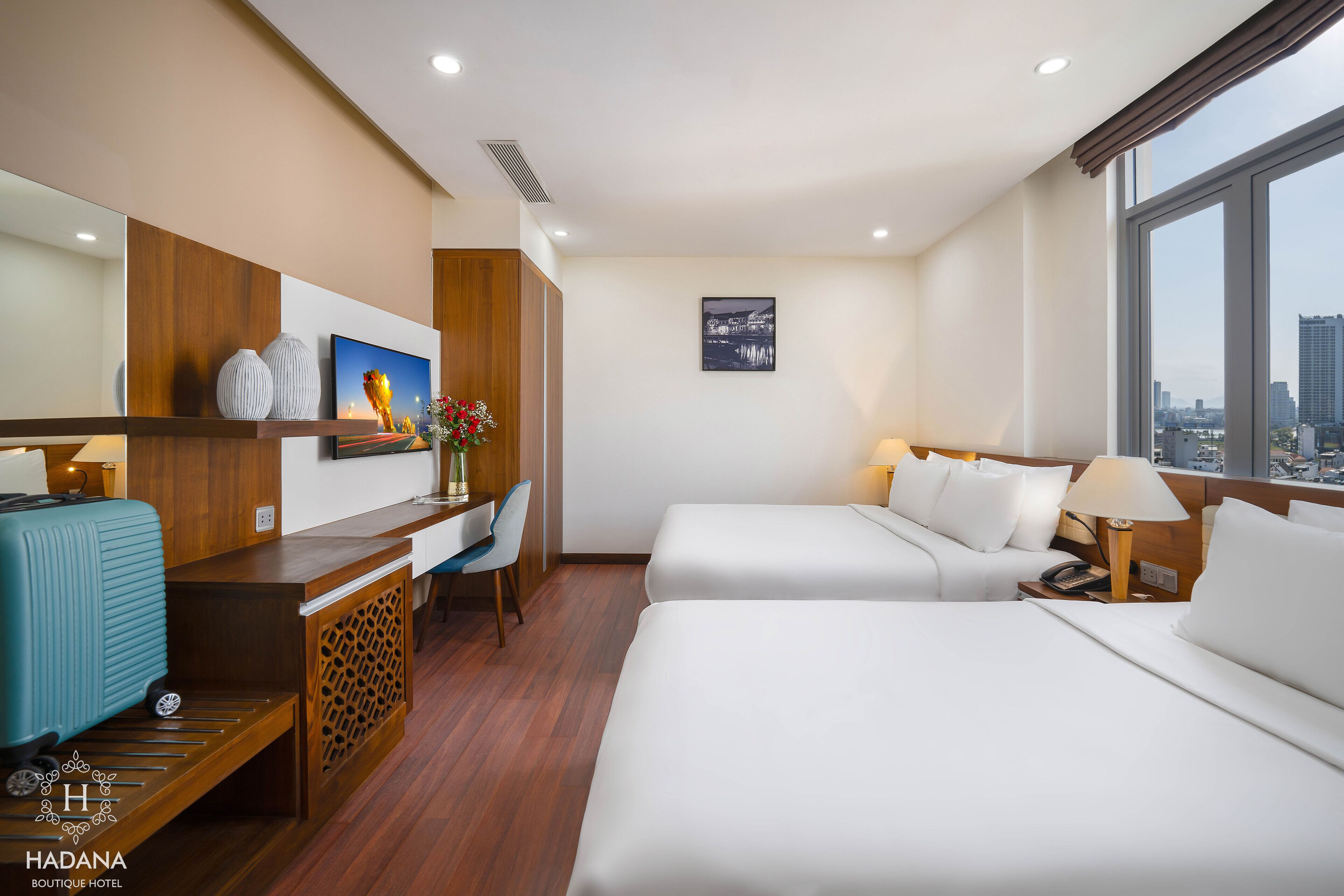 A hotel room with a desk, two beds, a city view, and a mounted artwork.