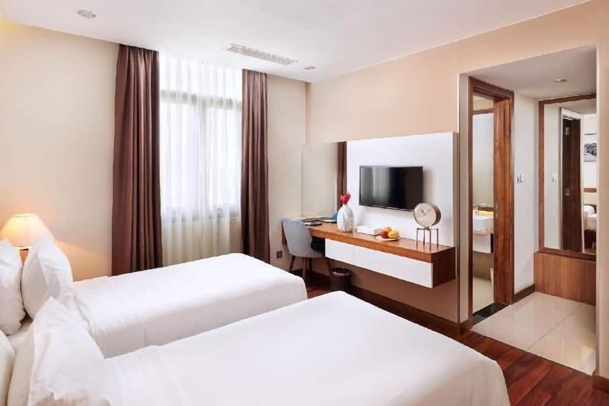A hotel room with two beds, a desk with a computer, a TV, and a mirror.