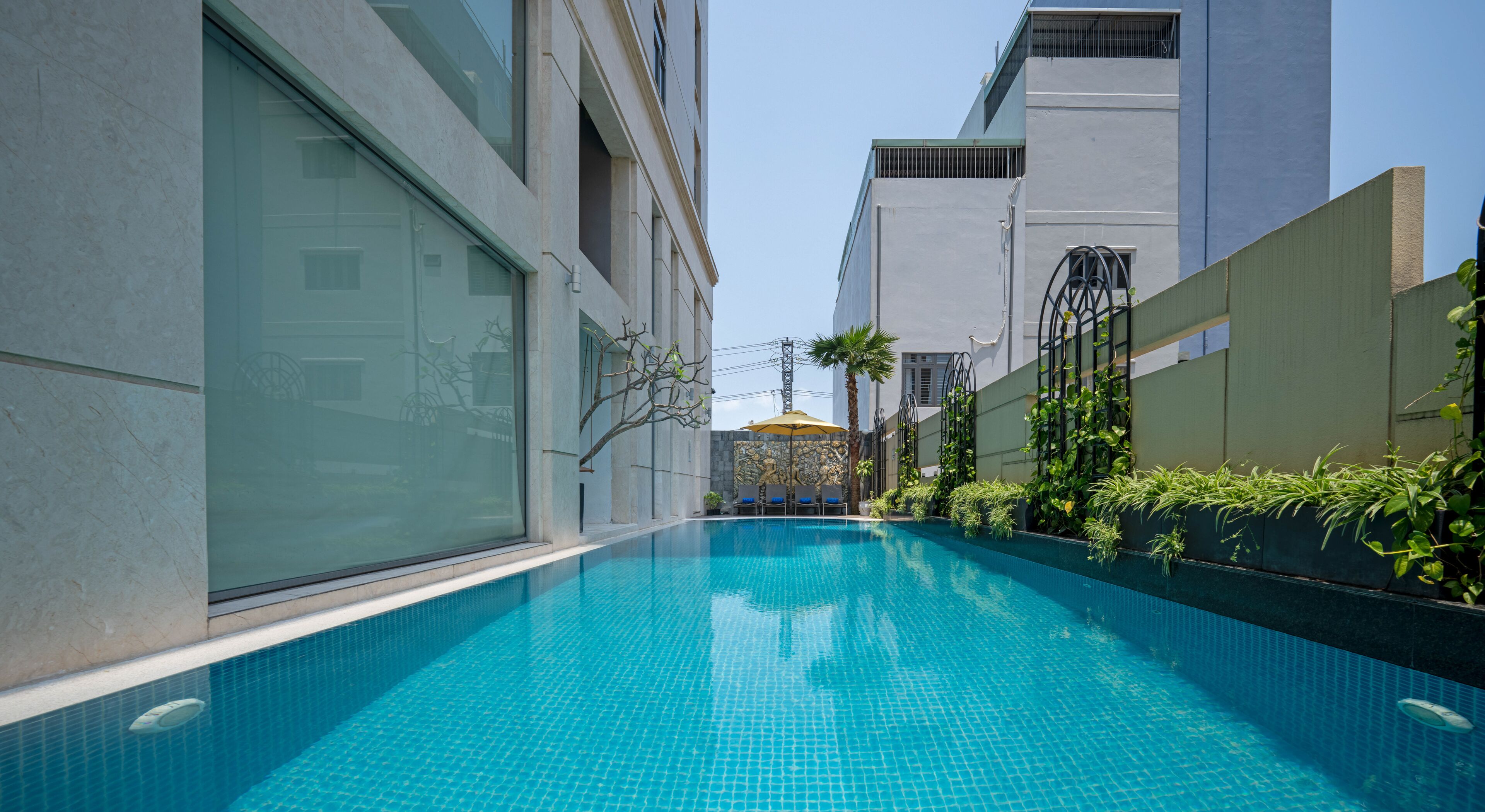 A modern swimming pool with clear blue water, surrounded by tall buildings and greenery.