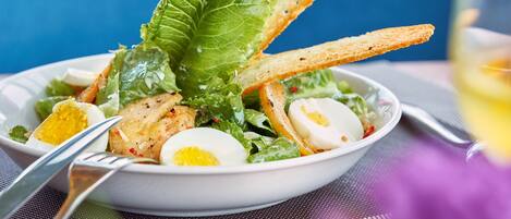 A bowl of salad with lettuce, eggs, and croutons on a table.