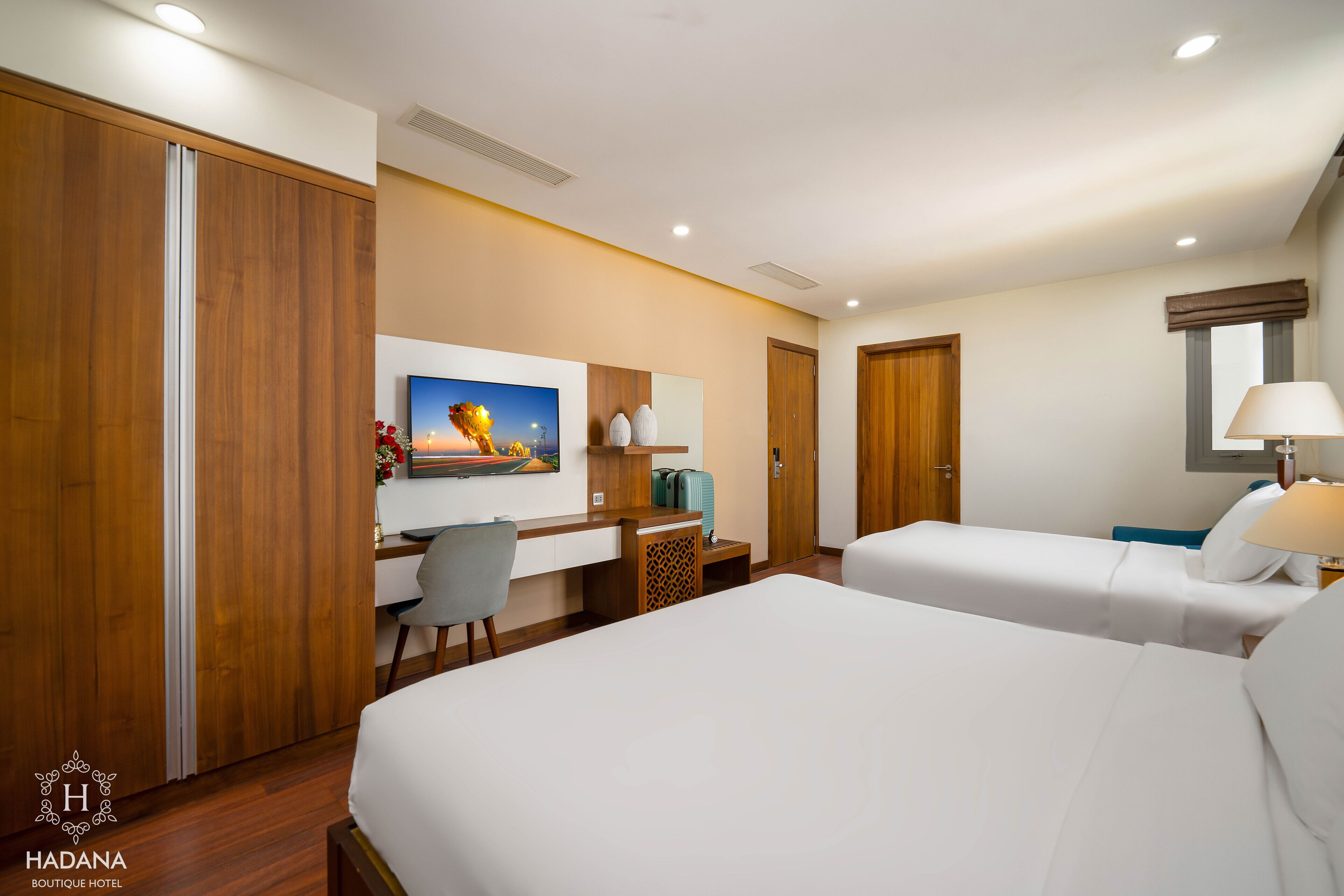 Habitación de hotel con dos camas, un escritorio, una silla, un televisor y una lámpara.
