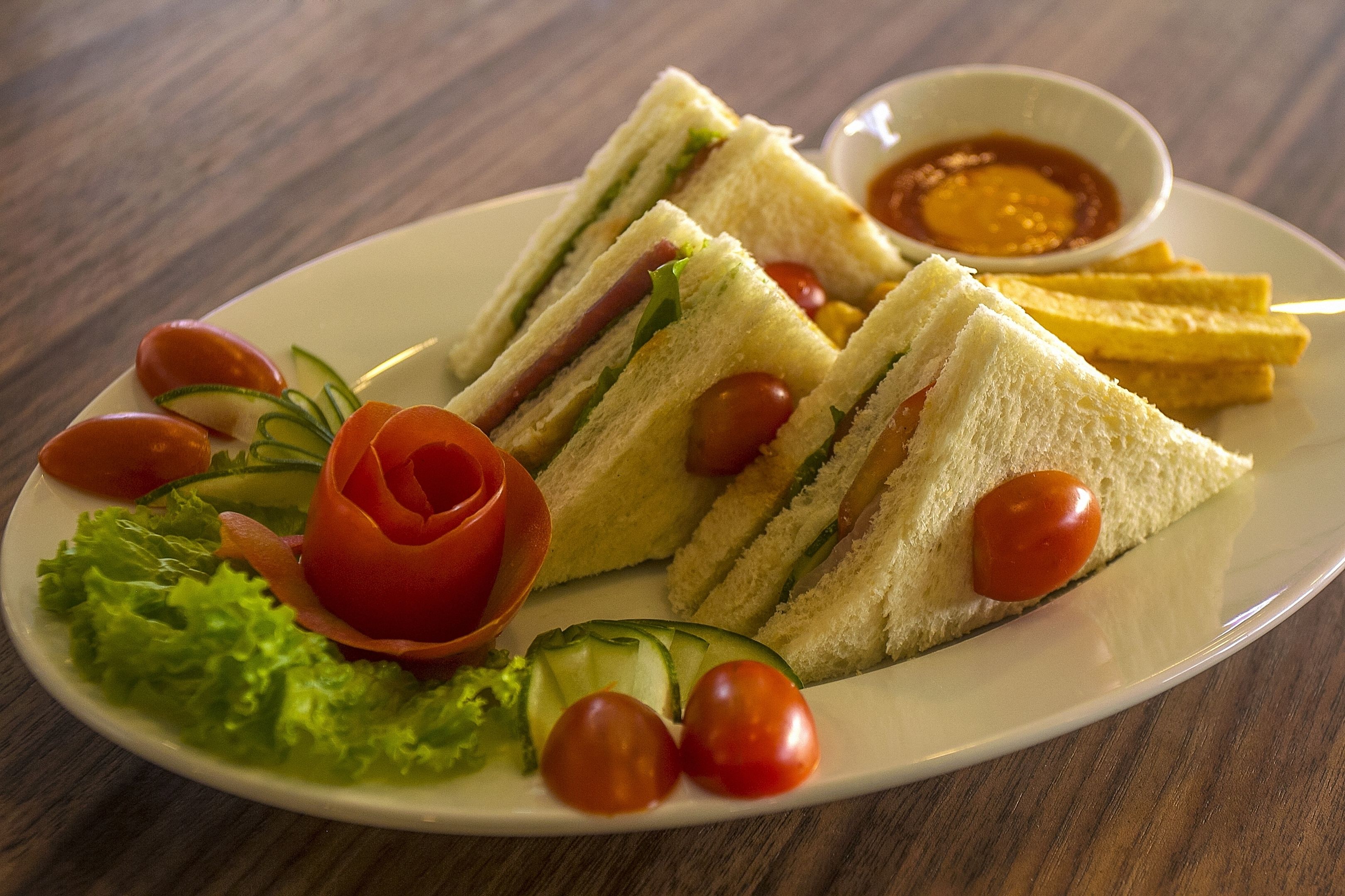 A plate with sandwiches, tomatoes, lettuce, and a small bowl of sauce.