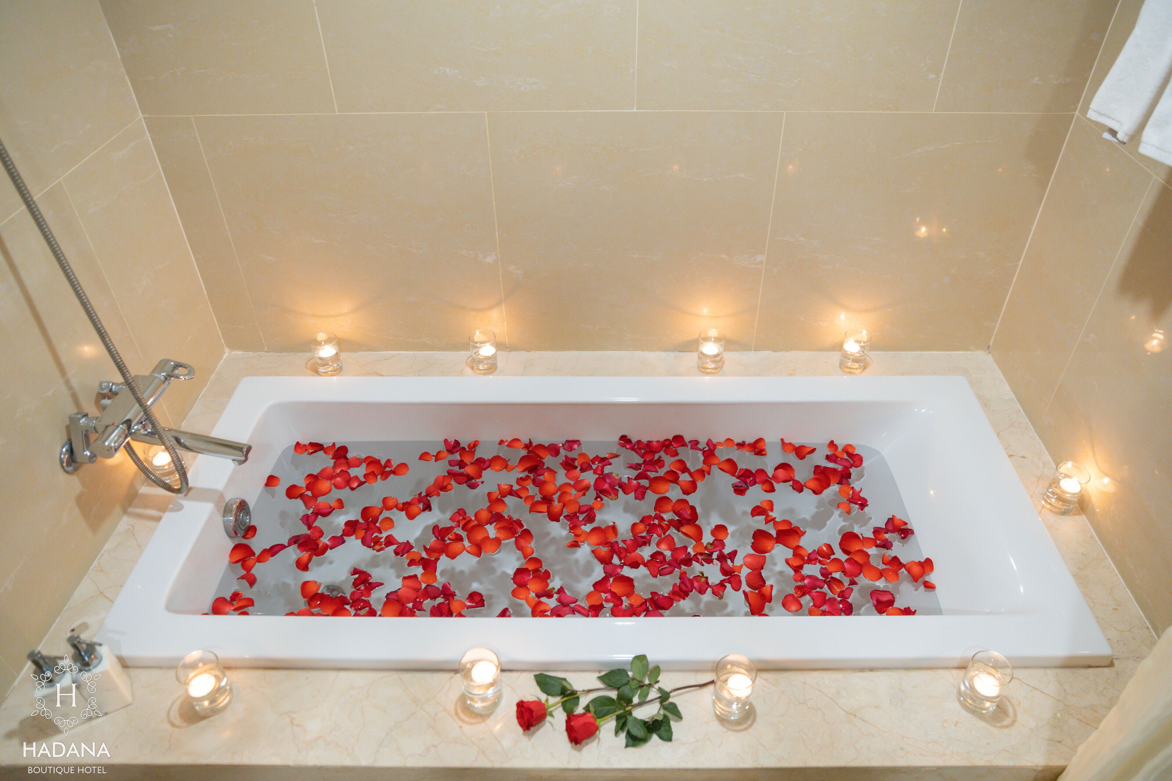 A bathtub filled with rose petals and lit candles, with a rose on the edge.