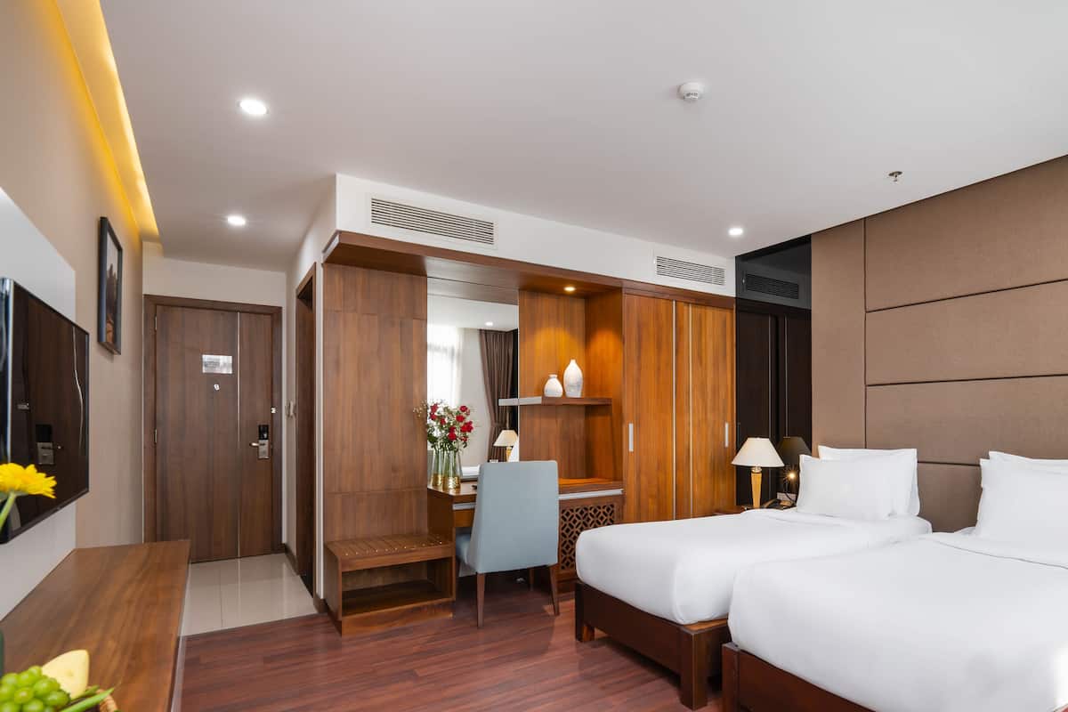 A hotel room with two beds, a desk, a chair, a TV, and a wardrobe.