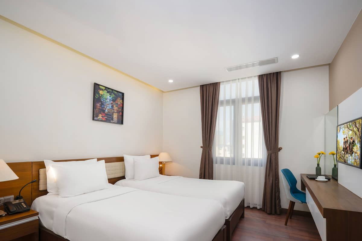 A hotel room with two beds, a desk, a chair, a lamp, a phone, and a painting on the wall.