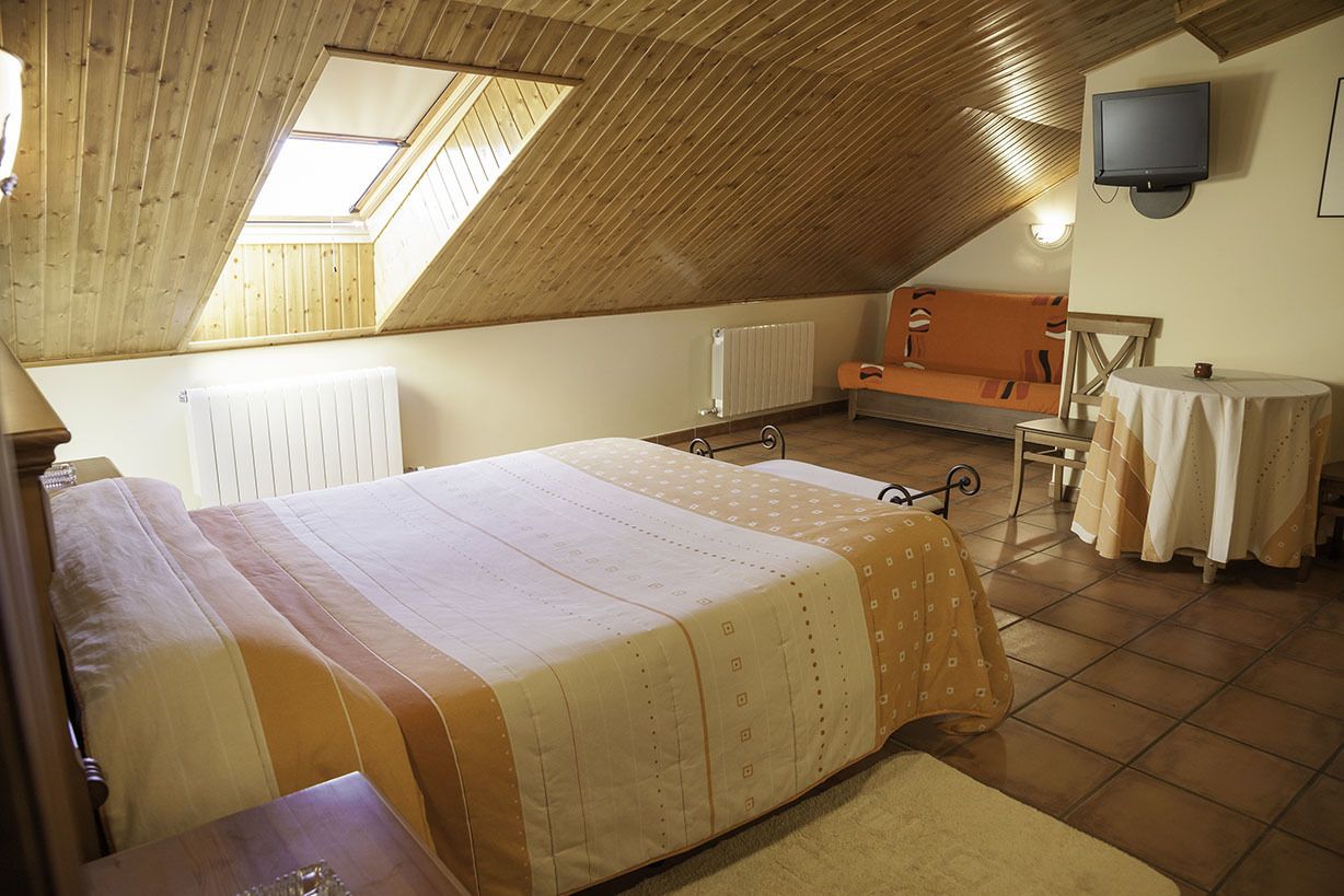 Un dormitorio acogedor en el ático, con techo inclinado, una cama, una mesita, una silla y un televisor en la pared.