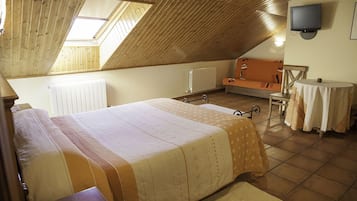 Un dormitorio acogedor en el ático, con techo inclinado, una cama, una mesita, una silla y un televisor en la pared.