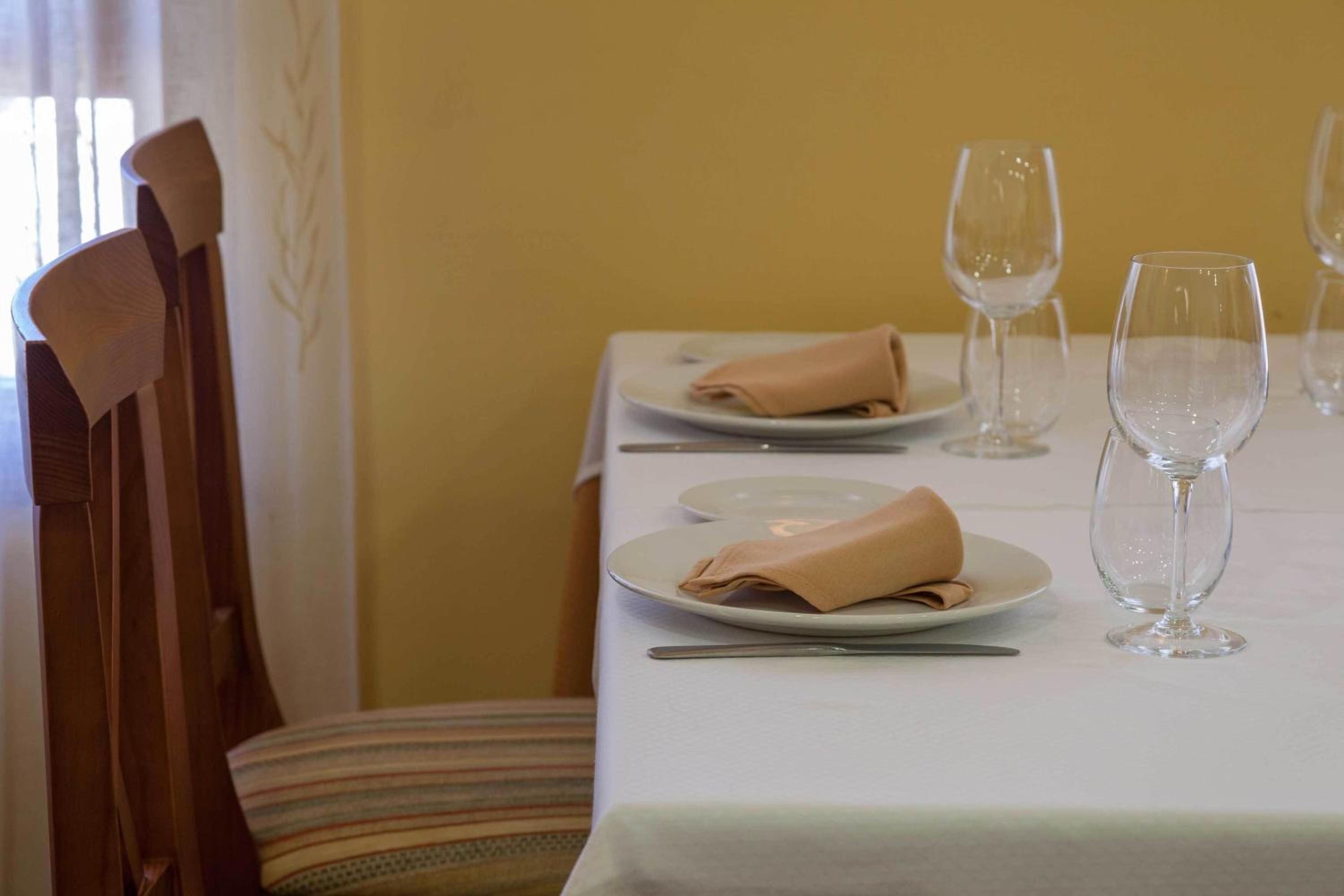 Una mesa de comedor dispuesta con platos, servilletas dobladas y copas de vino, con una silla a la izquierda.