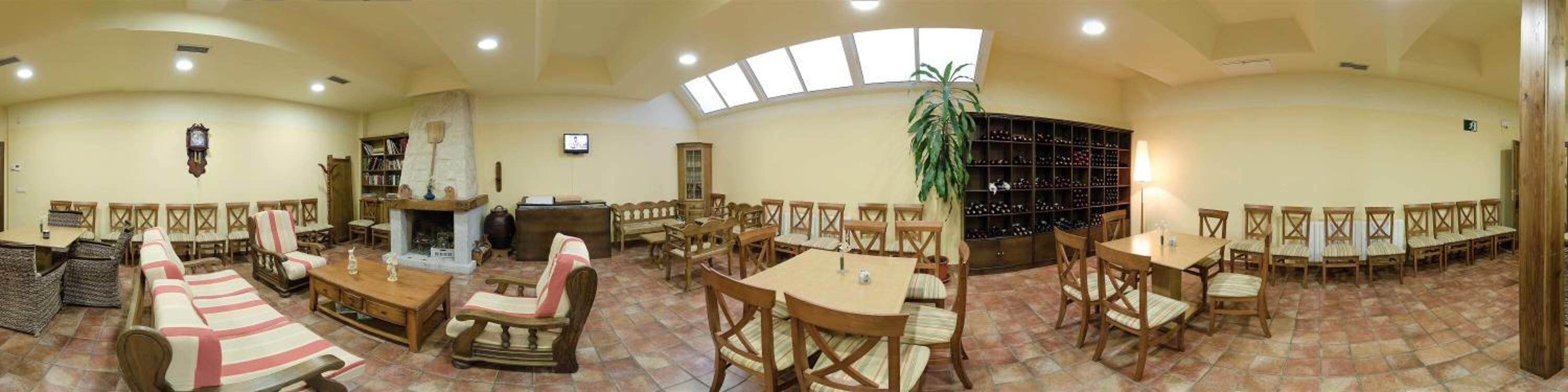 A spacious room with multiple seating areas, including sofas, chairs, and tables. There is a fireplace, a television, and a large plant.