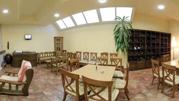 A spacious room with multiple seating areas, including sofas, chairs, and tables. There is a fireplace, a television, and a large plant.