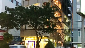 A multi-story building with balconies, a tree in front, and a street with moving vehicles. - Quan Quan Hotel (Da Nang)