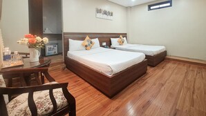 A hotel room with two beds, a wooden floor, a desk with a chair, and a vase with flowers. - Quan Quan Hotel (Da Nang)