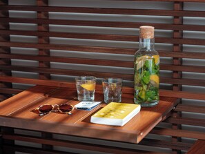 A wooden table with a bottle of water, two glasses, a pair of sunglasses, and a book.