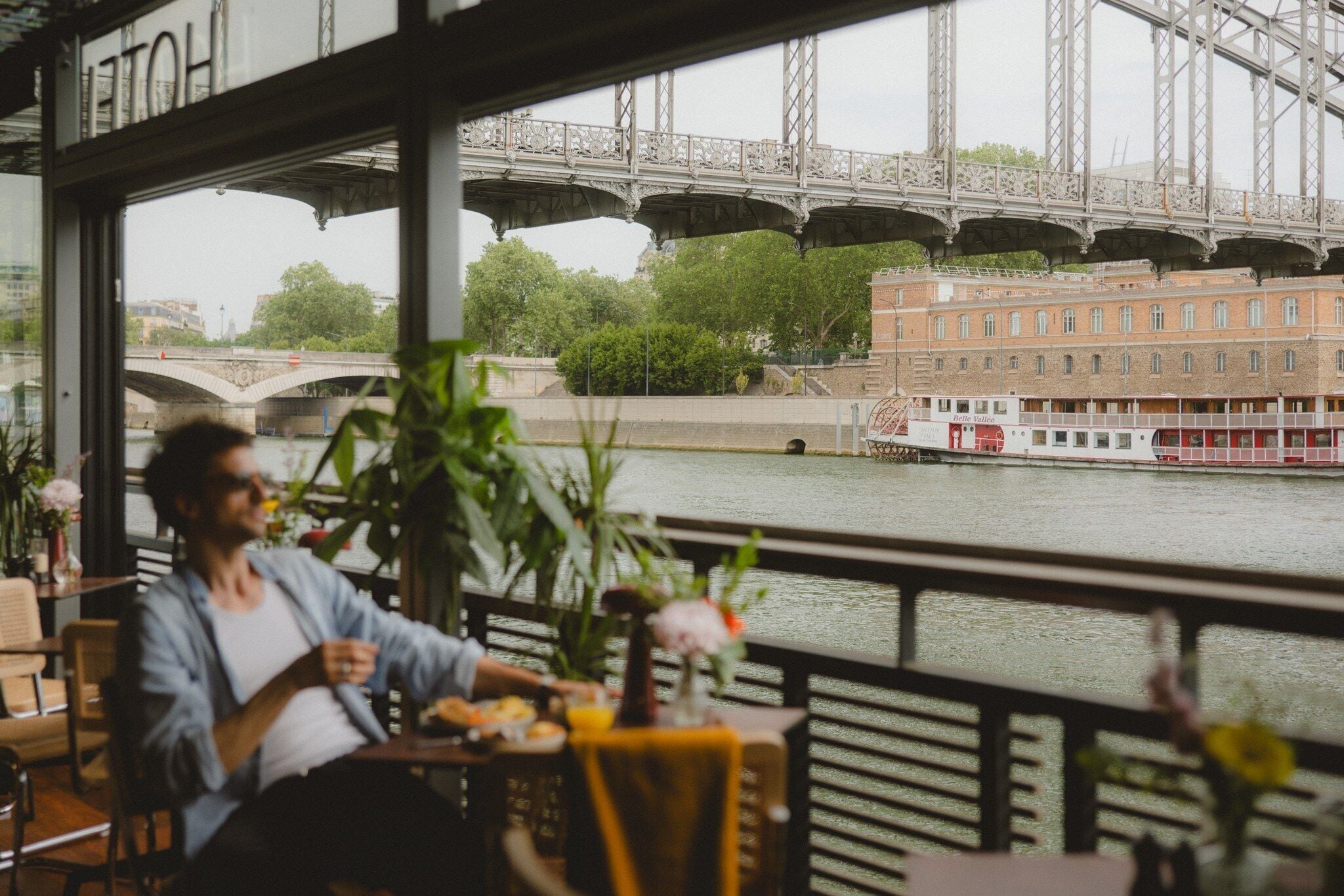Une personne assise à une table, avec vue sur une rivière et un pont.