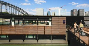 A modern building with a wooden facade, large windows, and a view of a bridge and city skyline.