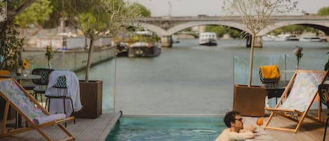 Zona de piscina con sillones de descanso y vistas a un puente y barcos.