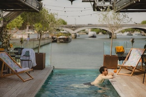 A pool area with lounge chairs and a view of a bridge and boats. - Off Paris Seine (Paris)