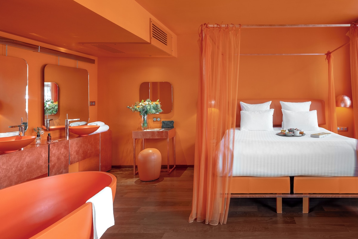 A modern hotel room with a large bed, a bathroom with a large mirror, and a vanity with two sinks.