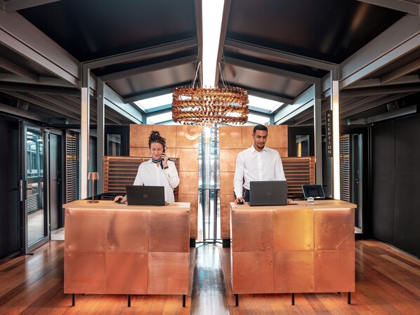 A reception area with two staff members at desks, a chandelier, and a modern interior design. - Off Paris Seine (Paris)