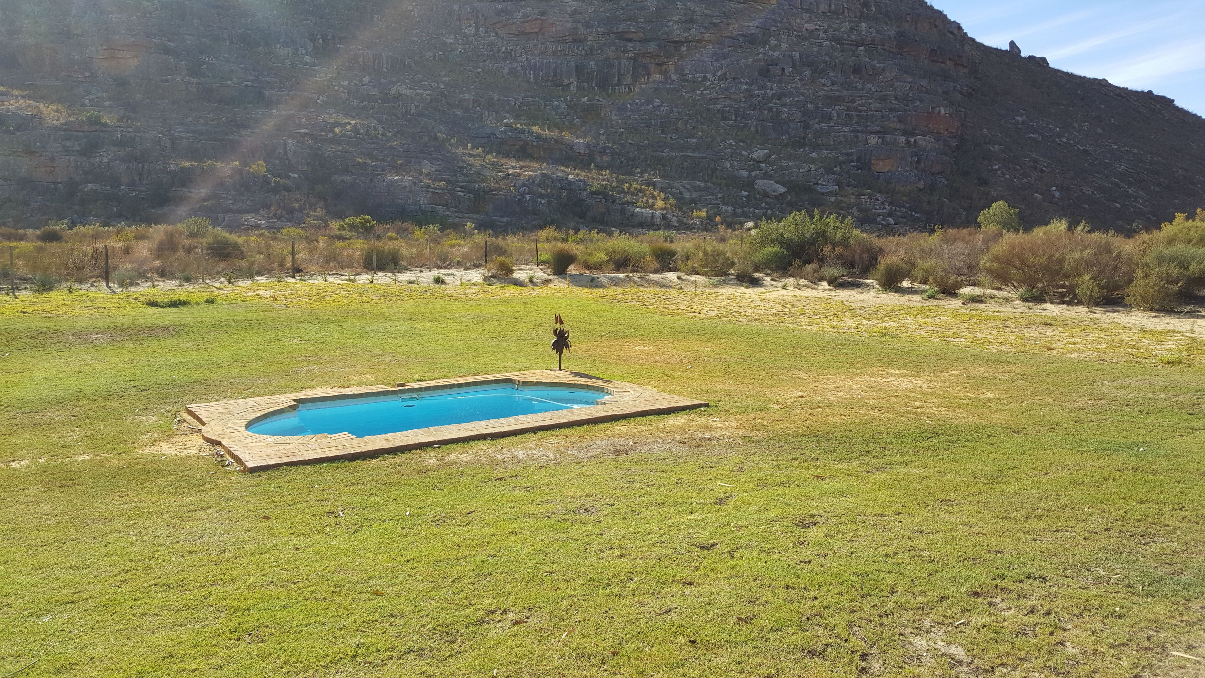 A swimming pool in a grassy field with a mountainous backdrop.