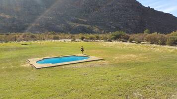 A swimming pool in a grassy field with a mountainous backdrop.