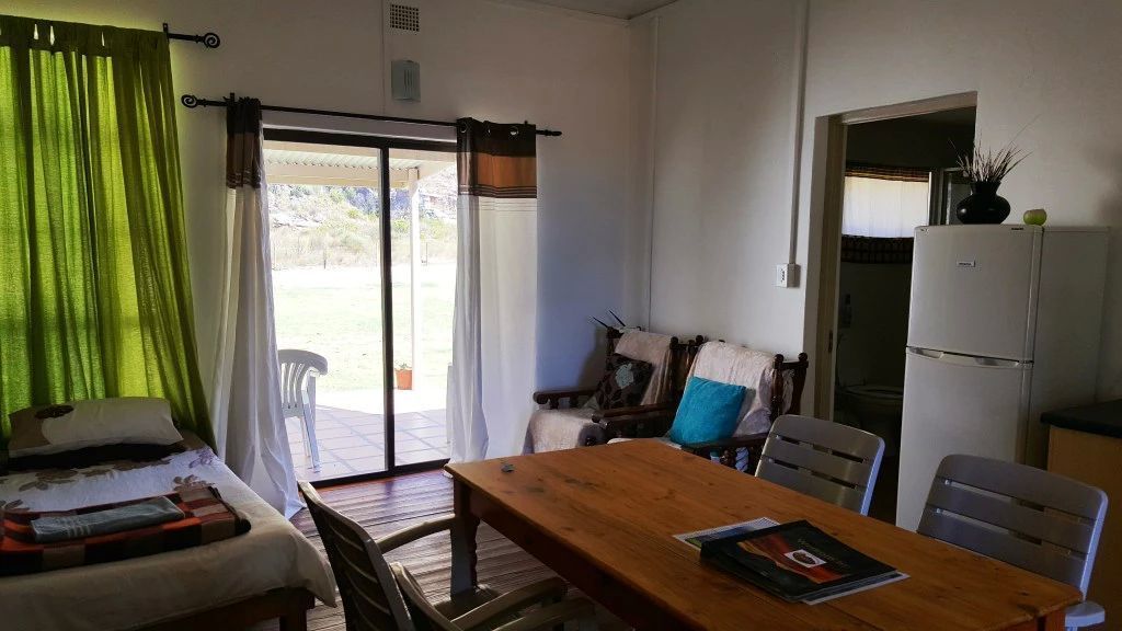 A room with a bed, a wooden table, a chair, a sofa, a refrigerator, and a sliding glass door leading to an outdoor area.