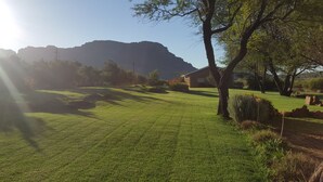 A grassy area with a building, trees, and a mountain in the background. - de Pakhuys (Cederberg)