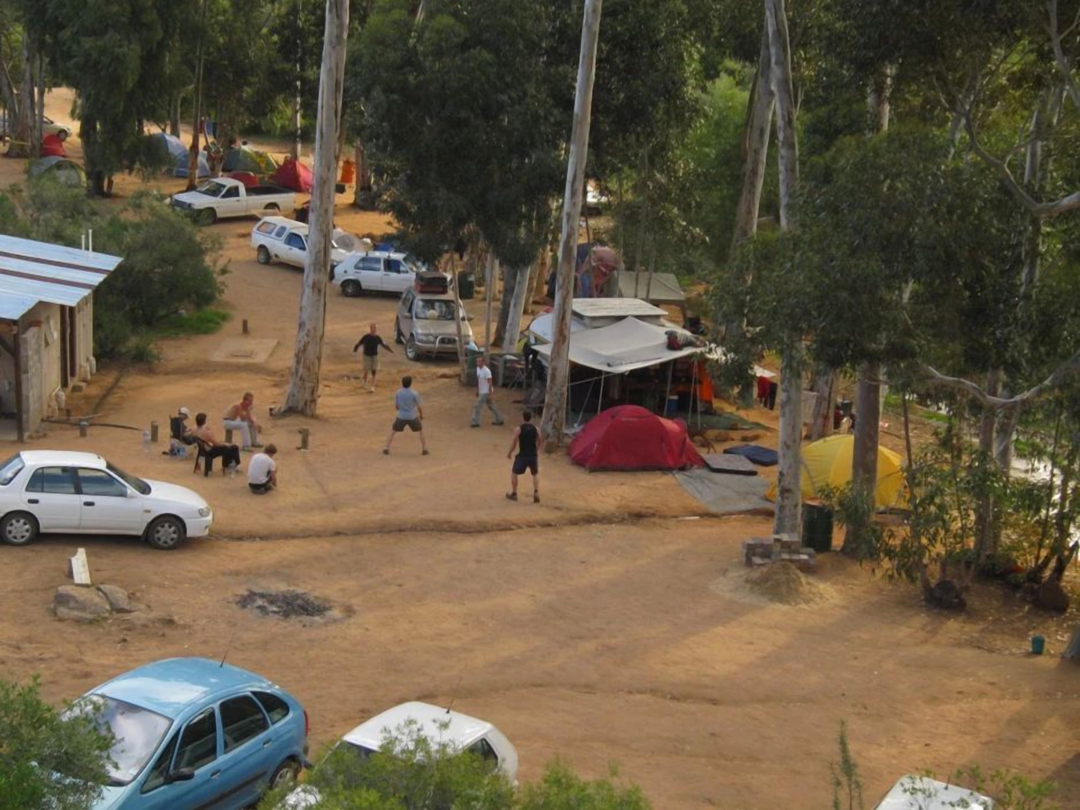 Un terrain de camping avec des tentes, des voitures et quelques personnes.