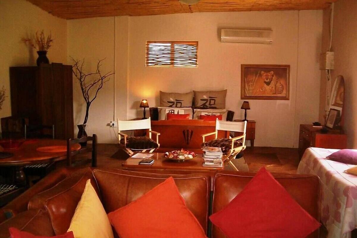A cozy living room with a leather sofa, a dining table with chairs, a fireplace, and a painting on the wall.