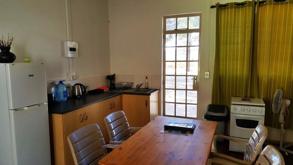 Een compacte keuken met een houten tafel, stoelen, een koelkast, een fornuis en een raam met gordijnen.
