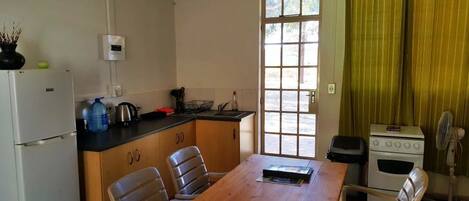 Een compacte keuken met een houten tafel, stoelen, een koelkast, een fornuis en een raam met gordijnen.