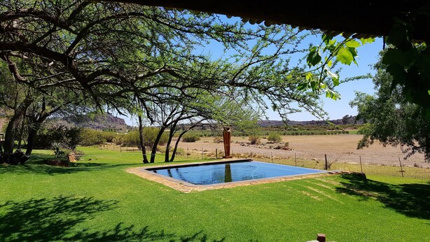 A swimming pool surrounded by lush green grass and trees, with a clear view of the surrounding landscape. - de Pakhuys (Cederberg)