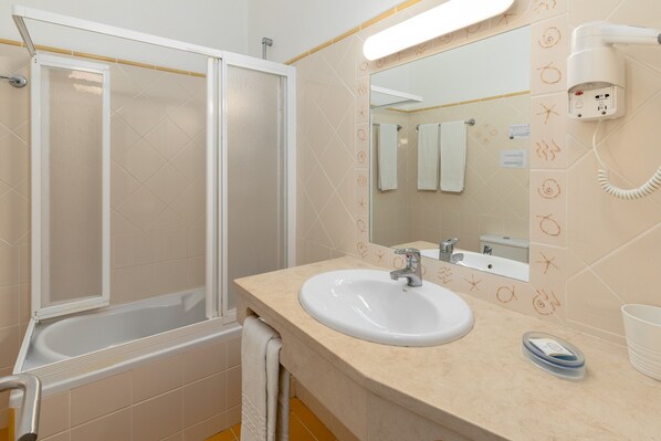 A bathroom with a bathtub, a sink, a mirror, and a hairdryer. - Villas Joinal (Albufeira)