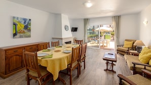 Un coin repas avec une table dressée pour quatre personnes, des chaises en bois, un téléviseur fixé au mur et un tableau au-dessus de la table.