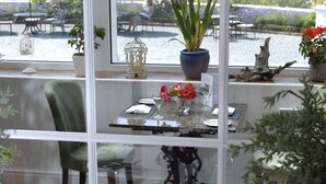 A dining area with a table set for two, a chair, and a view of a lake through large windows. - Plas Maenan Country House (Llanrwst)