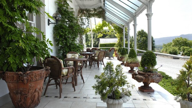 A covered patio area with wicker furniture, potted plants, and a view of the landscape. - Plas Maenan Country House (Llanrwst)