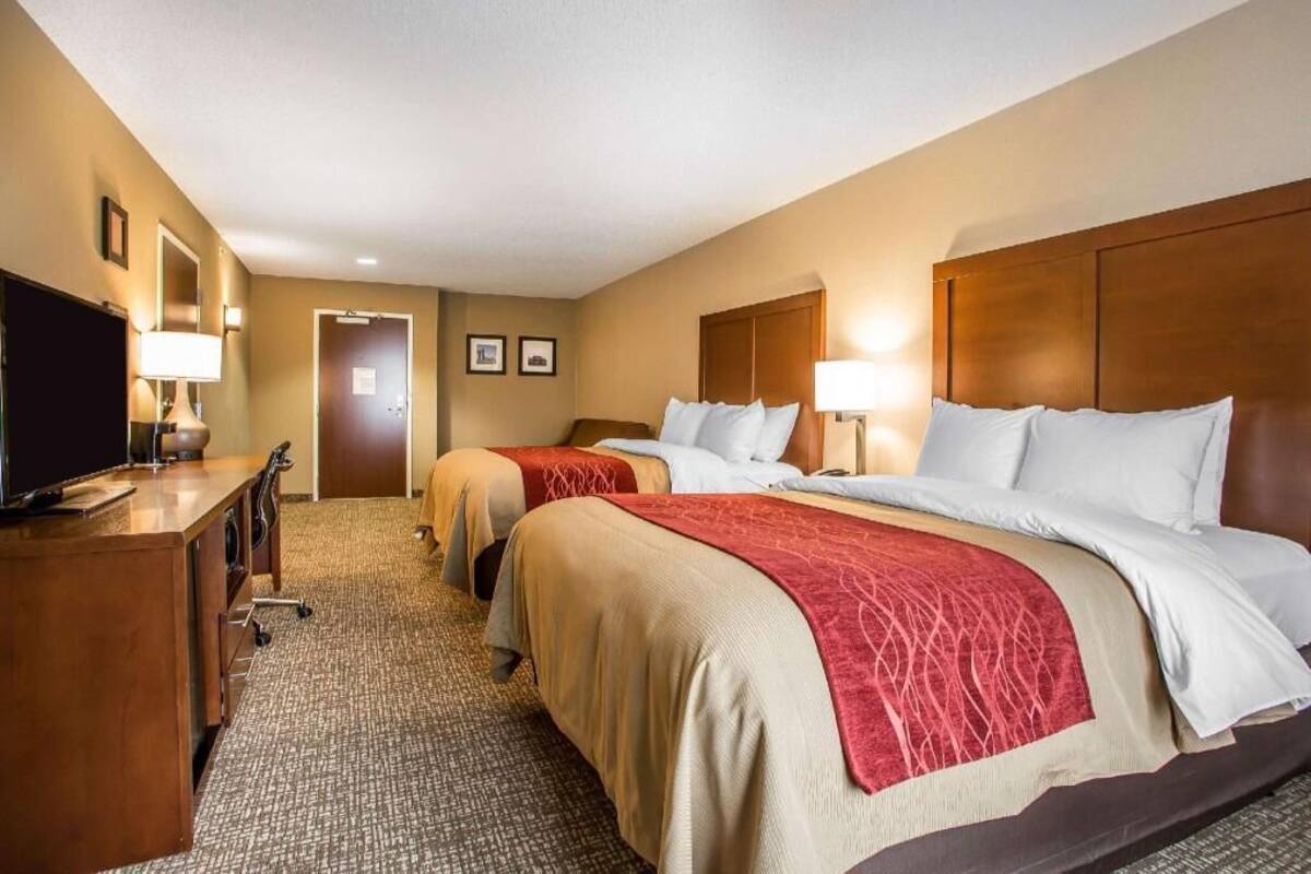 A hotel room with two beds, a desk, a TV, and a door.