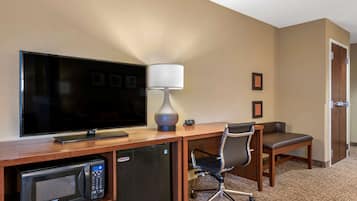 Et hotelværelse med et fladskærms-tv, et skrivebord med lampe, en mikrobølgeovn, en stol og et lille køleskab.