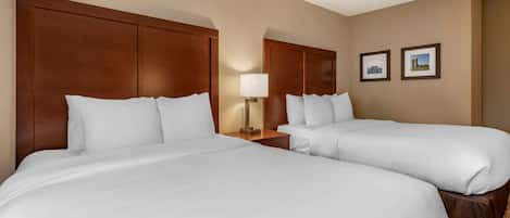 A hotel room with two beds, a nightstand with a lamp, and two framed pictures on the wall.