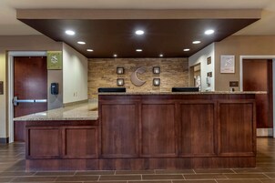 Un área de recepción con un mostrador de madera, una gran decoración mural en forma de C y un reloj en la pared.