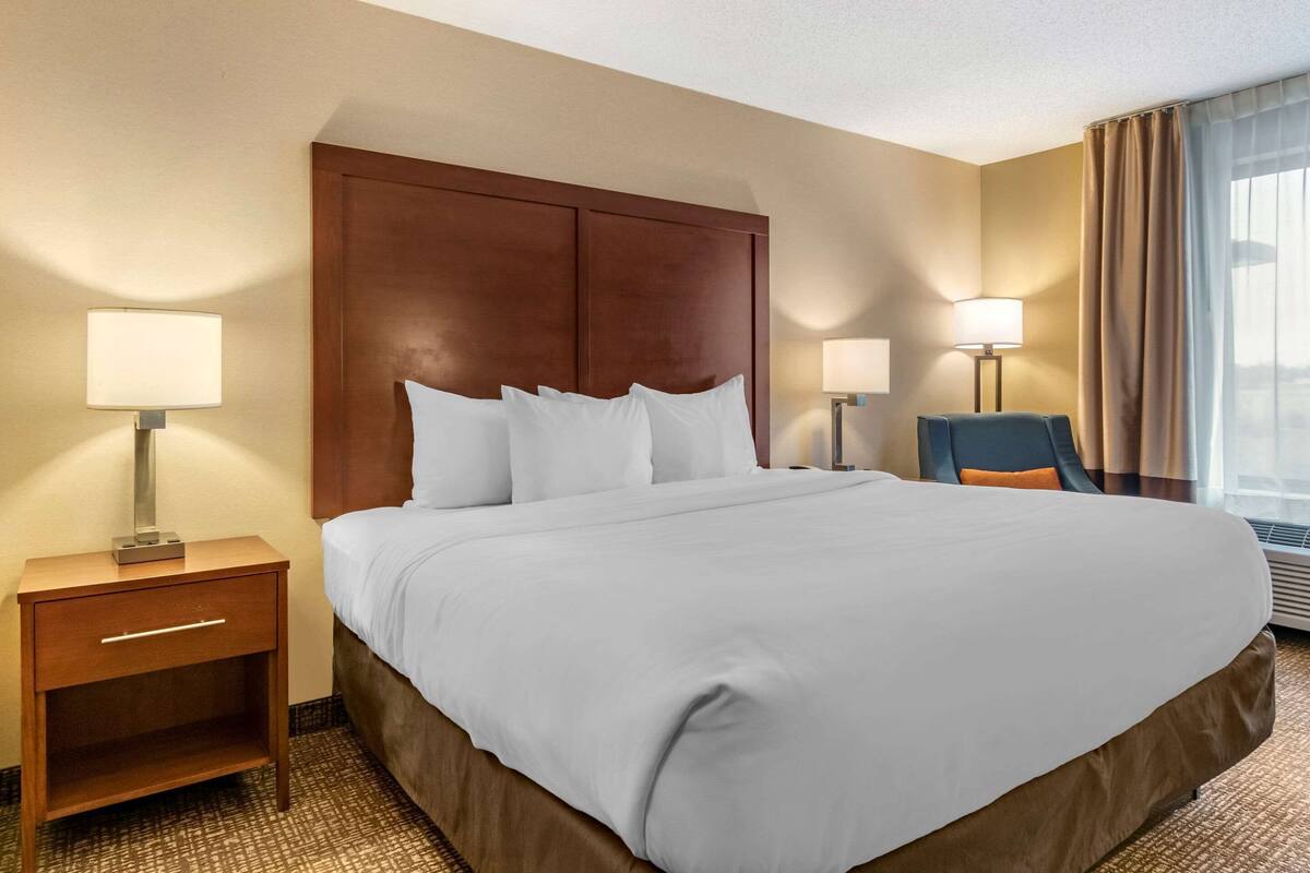 A hotel room with a large bed, two bedside tables with lamps, a chair, and a window with curtains.