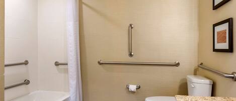 A bathroom with a bathtub, toilet, and handrails.