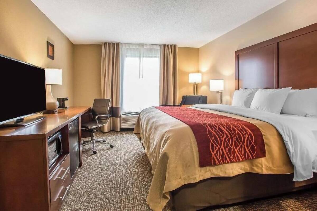 A hotel room with a bed, desk, chair, television, and lamps.