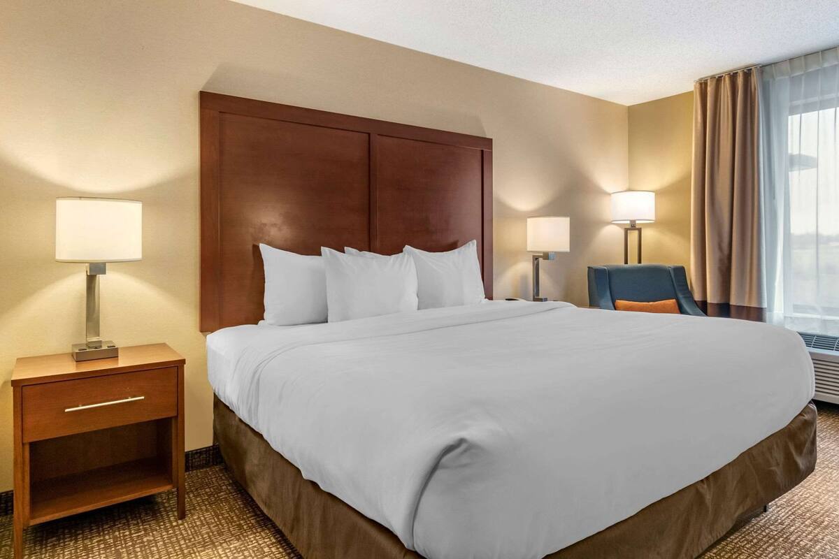 A hotel room with a large bed, two bedside tables with lamps, a chair, and a window with curtains.