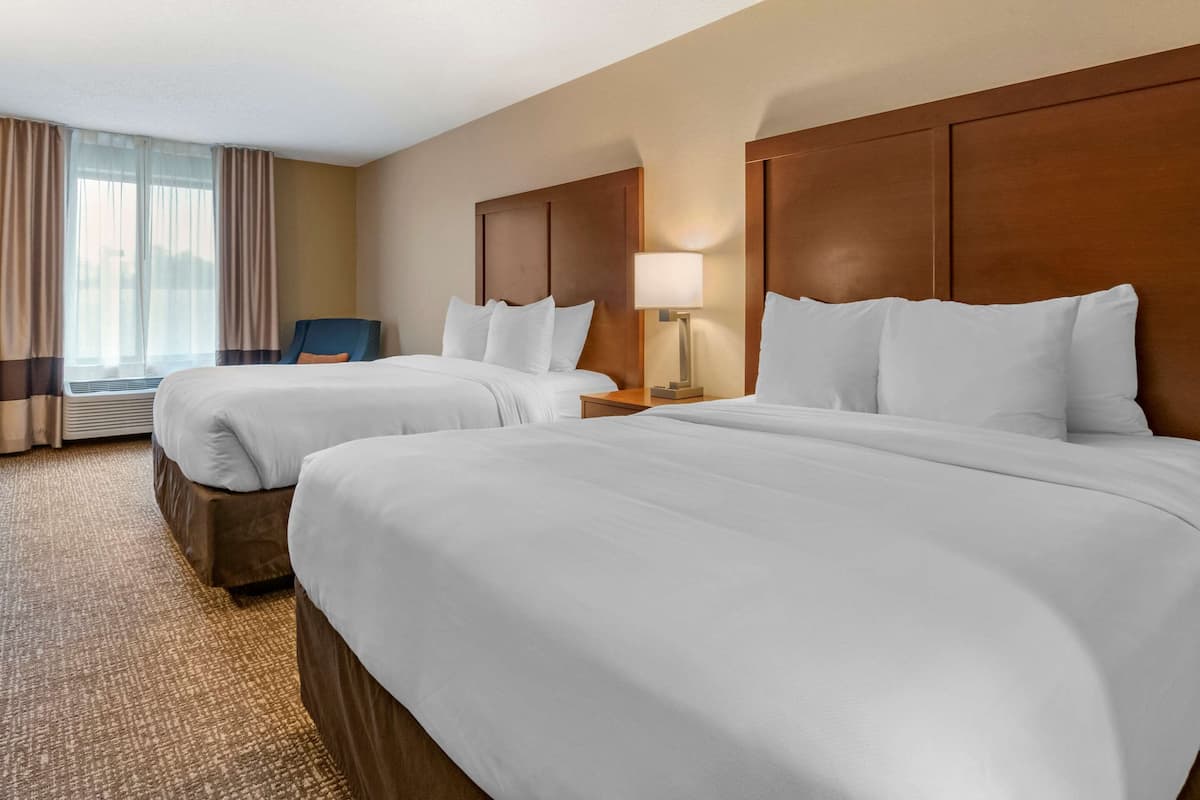 A hotel room with two beds, a chair, a lamp, and a large window with curtains.
